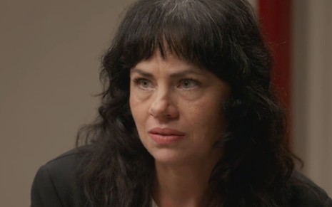 Karine Teles caracterizada como Carol; ela está séria em cena de Elas por Elas