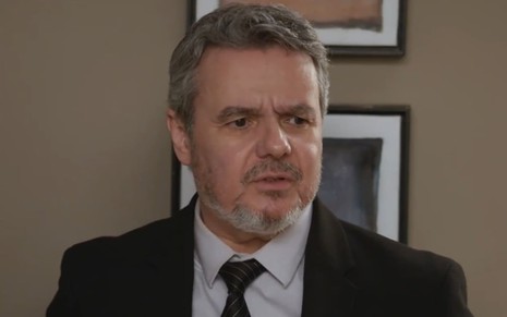 O ator Cassio Gabus Mendes com expressão preocupada, de terno e gravata, em cena de Elas por Elas