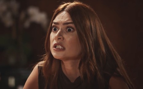Thaila Ayala caracterizada como Elisa; ela está com os olhos arregalados e mostra os dentes, em agonia, durante cena de Família É Tudo