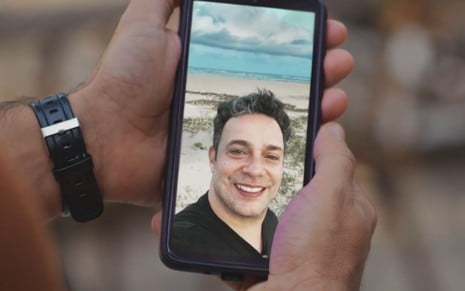 O ator Marcelo Médici como Ubaiara numa foto em um celular em cena de Família É Tudo