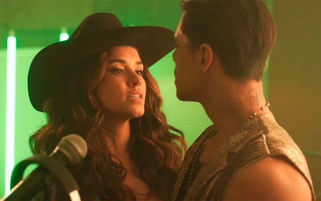 Talita Younan caracterizada como Selena; ela usa um chapéu de cowboy e dá um sorriso provocante enquanto encara Jefinho (Micael Borges) --fora do quadro--cena de Fuzuê
