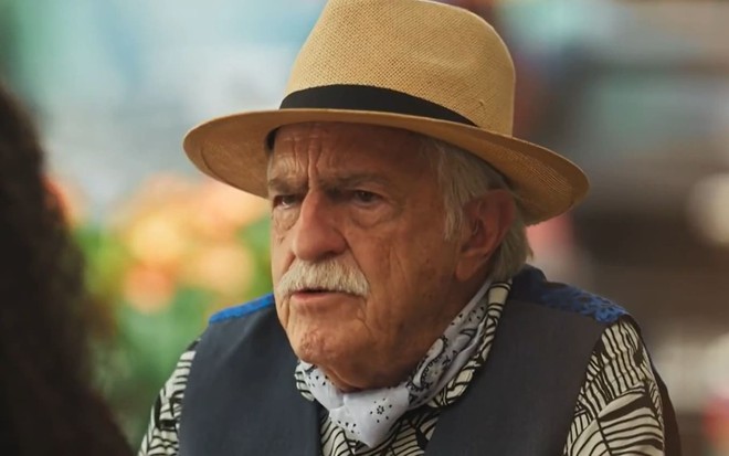 Ary Fontoura caracterizado como Lampião; ele usa um colete azul e um chapéu de palha e está sério em cena de Fuzuê