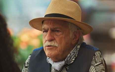 Ary Fontoura caracterizado como Lampião; ele usa um colete azul e um chapéu de palha e está sério em cena de Fuzuê