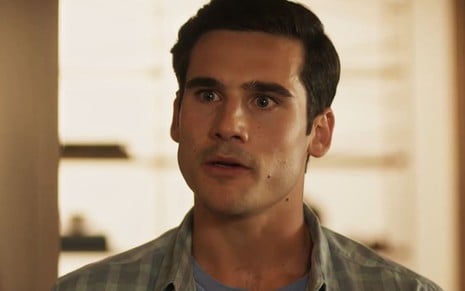 Nicolas Prattes caracterizado como Miguel; ele usa uma blusa camisa xadrez a parece transtornado em cena de Fuzuê