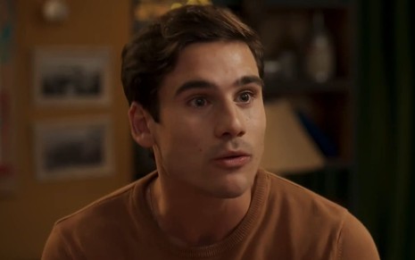 Nicolas Prattes caracterizado como Miguel; ele usa uma blusa bege e parece tenso em cena de Fuzuê