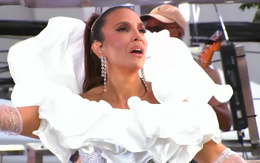 Ivete Sangalo faz careta em cima de trio elétrico; ela usa vestido branco com a gola bufante