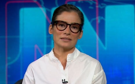 A apresentadora Renata Vasconcellos na bancada do Jornal Nacional com óculos de armação preta e uma blusa branca