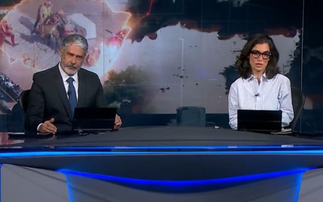 William Bonner à esquerda, emocionado, com Renata Vasconcellos à direita na bancada do Jornal Nacional