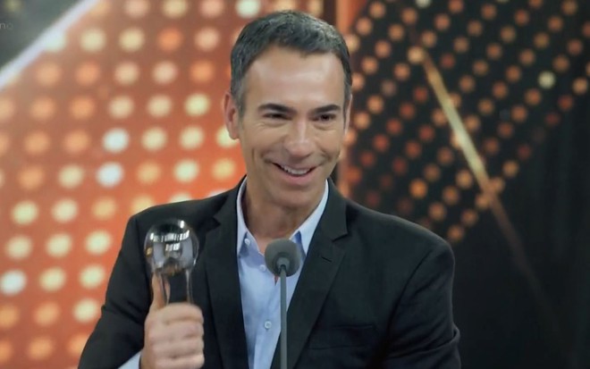 César Tralli sorri e mostra estatueta do Melhores do Ano no palco do Domingão