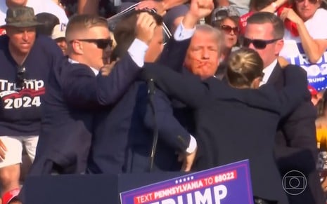 Donald Trump ergue o punho em gesto de luta; seu rosto está ensaguentado