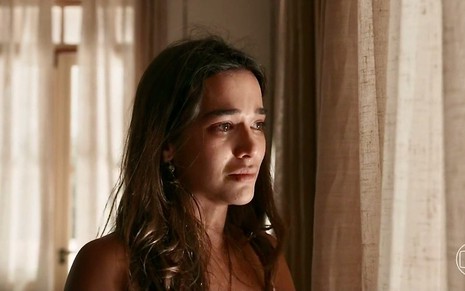 A atriz Theresa Fonseca tem cabelos soltos e está triste em cenário de Renascer, novela das nove da Globo