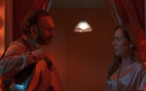 Almir Sater segura um violão e encara Camila Morgado em cena de Renascer que tem um filtro vermelho estourado