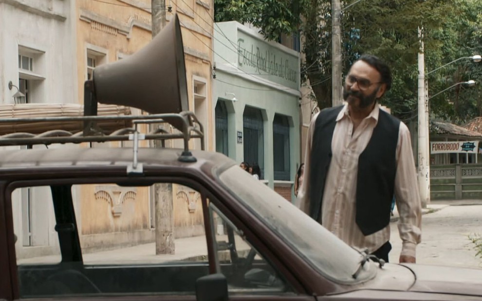O ator Almir Sater como Rachid em frente a um carro com um alto-falante