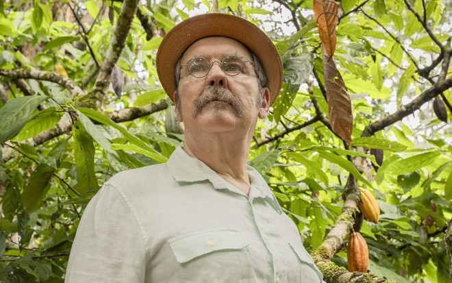 Antonio Calloni está com camisa clara e usa chapéu e óculos ao posar em uma mata como o coronel Belarmino do remake de renascer