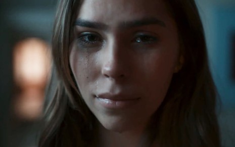 Gabriela Medeiros caracterizada como Buba; ela chora em frente a um espelho em cena de Renascer