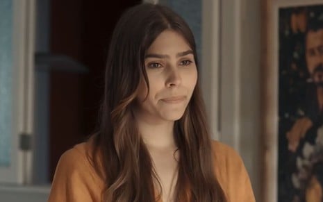 Gabriela Medeiros caracterizada como Buba; ela usa um vestido laranja e está séria em cena de Renascer