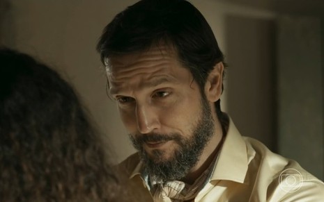 O ator Vladimir Brichta está encarando Alice Carvalho, de costas e cortada na imagem, em cena da novela Renascer