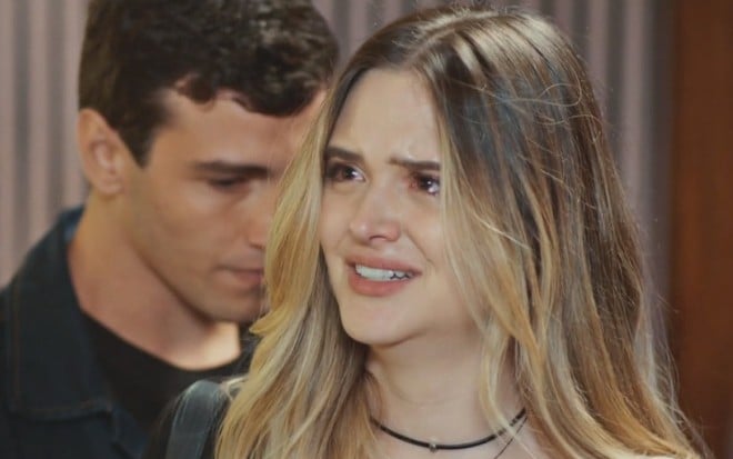 A atriz Juliana Paiva está chorando em cena de Família É Tudo, com Henrique Barreira atrás dela