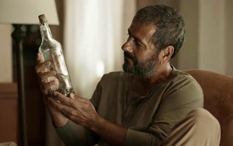 José Inocêncio (Marcos Palmeira) segura garrafa com cramulhãozinho em cena da novela Renascer