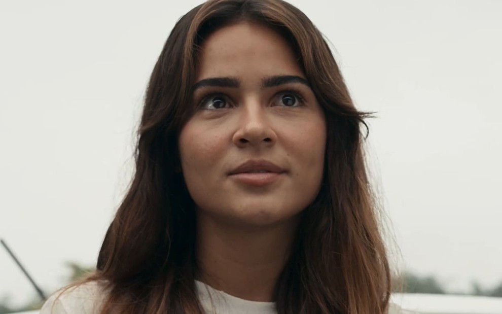 Giullia Buscacio caracterizada como Sandra; ela dá um sorriso irônico em cena de Renascer