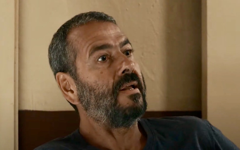 O ator Marcos Palmeira está sentado e olha para alguém à frente dele em cena da novela Renascer