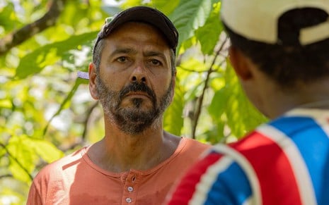O ator Marcos Palmeira, de boné e camisa vermelha, em uma lavoura de cacau como José Inocêncio em cena de Renascer