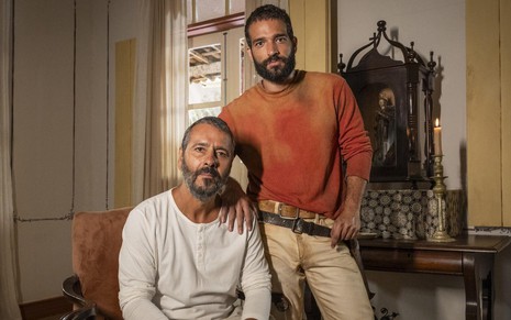 Marcos Palmeira está sentado, usa blusa branca de manga longa, e Humberto Carrão usa camiseta laranja; eles estão caracterizados como José Inocêncio