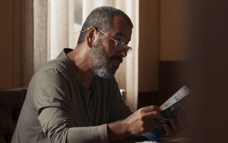 Marcos Palmeira como José Inocêncio utilizando um óculos para perto e lê uma revista em cena de Renascer