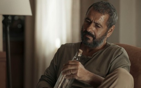O ator Marcos Palmeira caracterizado como José Inocêncio em cena de Renascer segurando uma garrafa de vidro