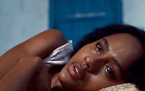 Duda Santos está deitada com olhar triste em cena como Maria Santa, a Santinha, do remake de Renascer