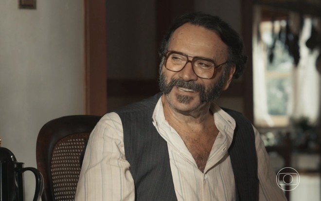 O ator Almir Sater está sorrindo caracterizado como Rachid em cena da novela Renascer, da Globo