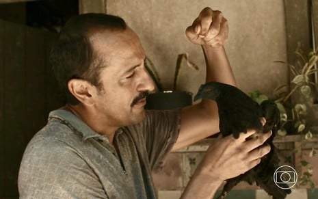 O ator Irandhir Santos segura uma galinha preta em cena da novela Renascer, da Globo, como Tião