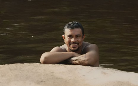 O ator Xamã nu em um rio como o Damião em cena do remake de Renascer