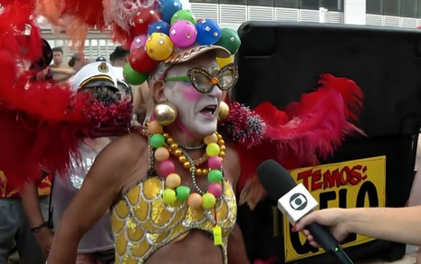 Um homem de cerca de 70 anos está vestido como uma drag queen, com maquiagem branca e bolas coloridas na Banda de Ipanema, no Rio