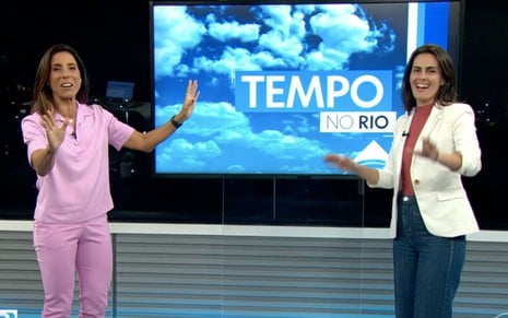 Mônica Teixeira, de rosa, ao lado de Priscila Chagas, de branco, em frente a um telão escrito Previsão do Tempo no RJ2