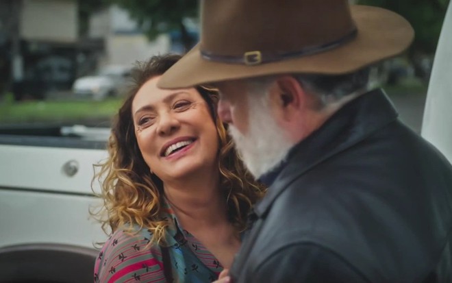 A atriz Eliane Giardini sorri e abraça Tony Ramos, que está de chapéu e jaqueta em cena de Terra e Paixão