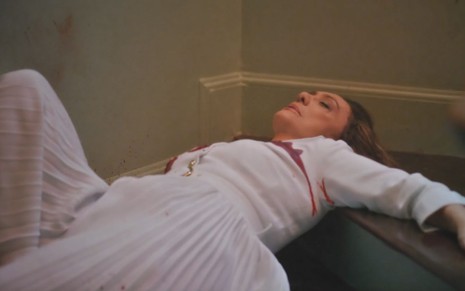 A atriz Eliane Giardini caída no chão com sangue no peito como a Agatha em cena de Terra e Paixão