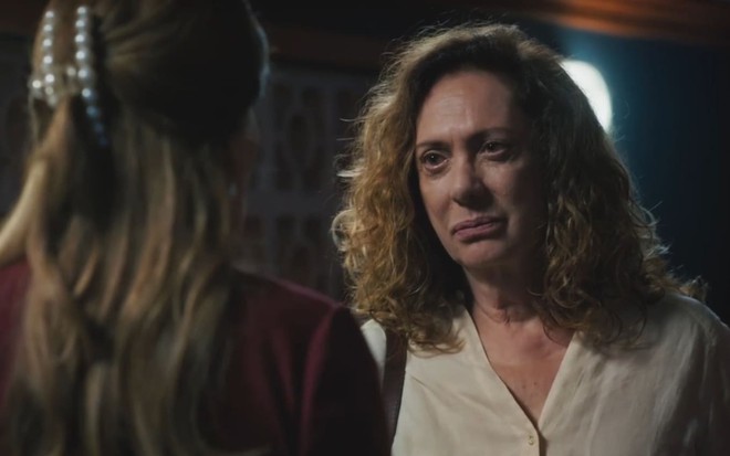Eliane Giardini caracterizada como Agatha; ela tem os cabelos curtos e cacheados, com poucas mechas loiras. A atriz usa uma camisa estampada e encara a câmera em ensaio de divulgação de Terra e Paixão