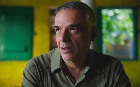 Ângelo Antônio caracterizado como Andrade; ele usa uma camisa cinza puída e parece abatido em cena de Terra e Paixão