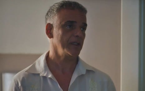Ângelo Antônio caracterizado como Andrade; ele usa uma camisa branca e parece tenso em cena de Terra e Paixão