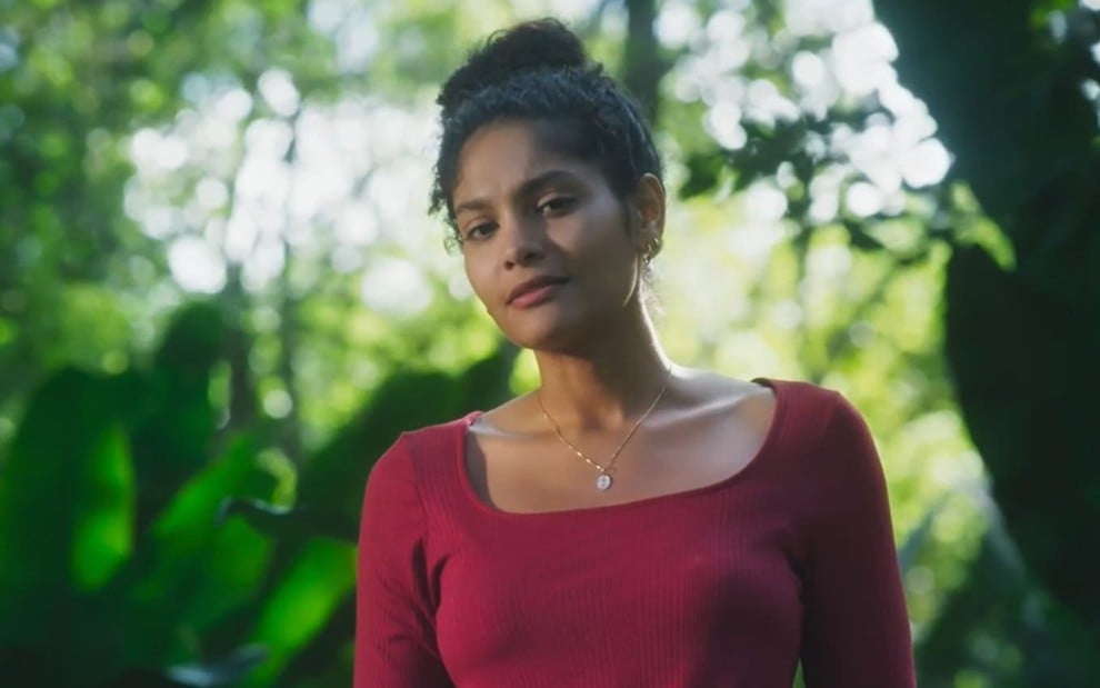 Barbara Reis caracterizada como Aline; ela usa uma camiseta verde e tem o semblante abalado em cena de Terra e Paixão