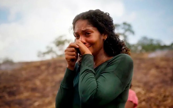 A atriz Barbara Reis usa blusa verde de manga longa e chora com mãos perto da boca em cena da novela Terra e Paixão