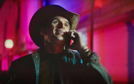 O ator Eriberto Leão usa chapéu e fala ao telefone em cena noturna da novela Terra e Paixão como Dirceu