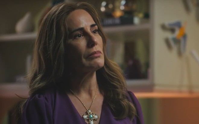 Gloria Pires caracterizada como Irene; ela usa uma camiseta roxa e estende o pescoço, imponente, em cena de Terra e Paixão