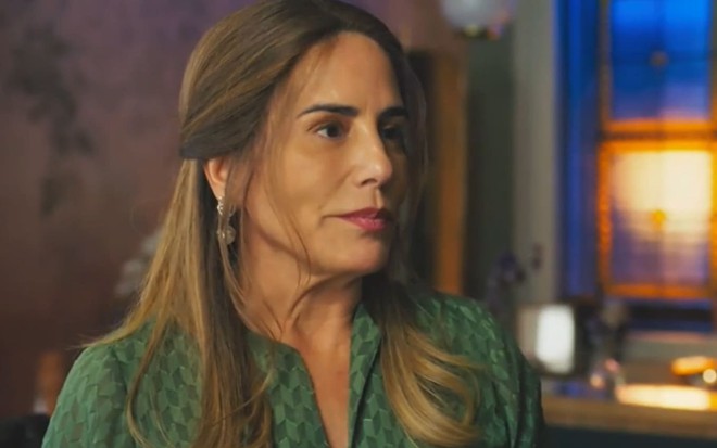 Gloria Pires caracterizada como Irene; ela está com os cabelos castanhos soltos e usa um vestido rosa. O semblante exprime fúria em cena de Terra e Paixão
