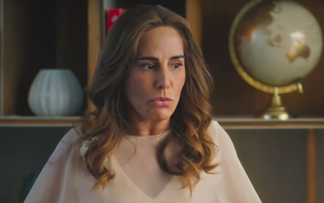 Gloria Pires caracterizada como Irene; ela usa uma blusa bege e parece abismada em cena de Terra e Paixão