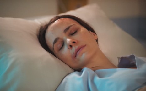A atriz Débora Falabella está deitada no leito de um hospital e simula dormir em cena da novela Terra e Paixão