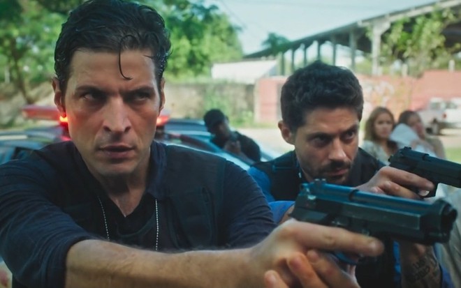 Leandro Lima em cena da novela Terra e Paixão, da Globo, como o delegado Marino; ele aponta uma arma junto com um figurante