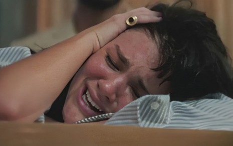 A atriz Debora Ozório está chorando com a mão na cabeça em cena da novela Terra e Paixão