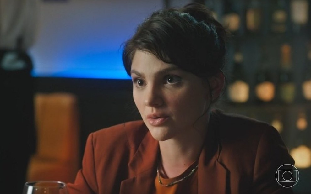 A atriz Debora Ozório usa cabelo preso e casaco vinho em cena da novela Terra e Paixão como a personagem Petra